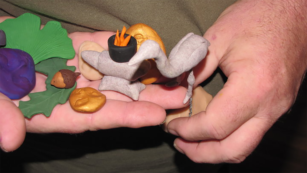 Two hand hold up small clay figureines: a fire, a leaf, a standing crane, and others.