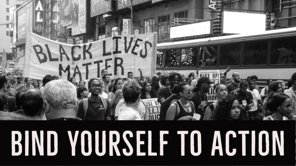 A black and white photo of marchers, some holding over their heads a large cloth banner reading "Black Lives Matter." Below the photograph, a legend in bold text: Bind Yourself to Action.