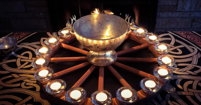 A ring of glowing candles surrounds a silver bowl, an offering to Brigando.